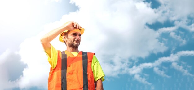 Um retrato de um trabalhador fica com confiança em um terno de trabalho laranja e capacete de segurança contra o céu Conceito de trabalho de trabalhador industrial inteligente