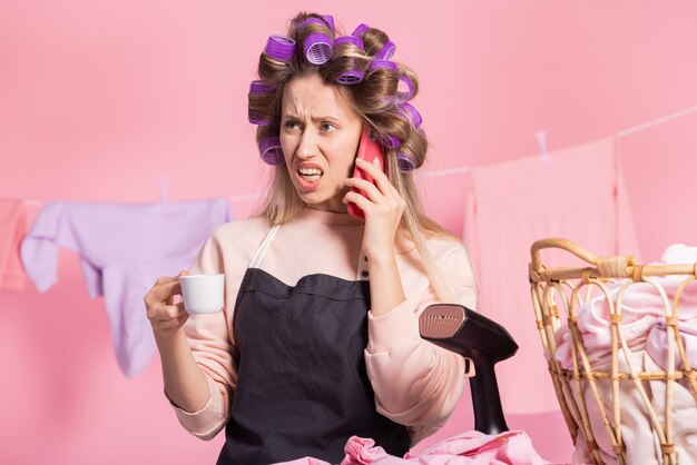 Um retrato de uma dona de casa falando ao telefone com uma cara de brava a mulher segura uma xícara de café