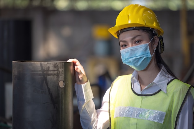 Um retrato de uma engenheira industrial com máscara em pé em uma fábrica.