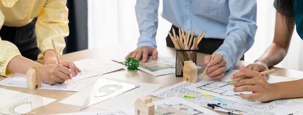 Um retrato de uma equipe de arquitetos profissionais discutindo um projeto arquitetônico em uma mesa de reunião com projeto e blocos de madeira espalhados em um escritório moderno Closeup Focus delineamento manual