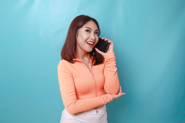 Um retrato de uma jovem asiática alegre tendo um telefonema isolado em fundo azul