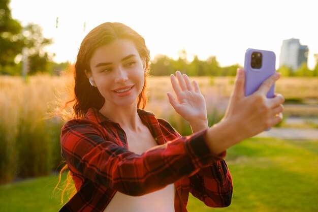 Um retrato de uma jovem blogueira ruiva feliz com uma camisa a quadros saúda calorosamente seus seguidores gravando