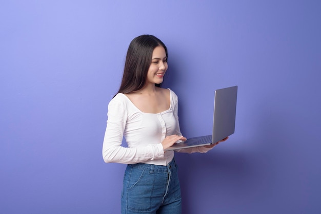 Um retrato de uma jovem linda e sorridente está segurando laptop sobre estúdio de fundo roxo isolado