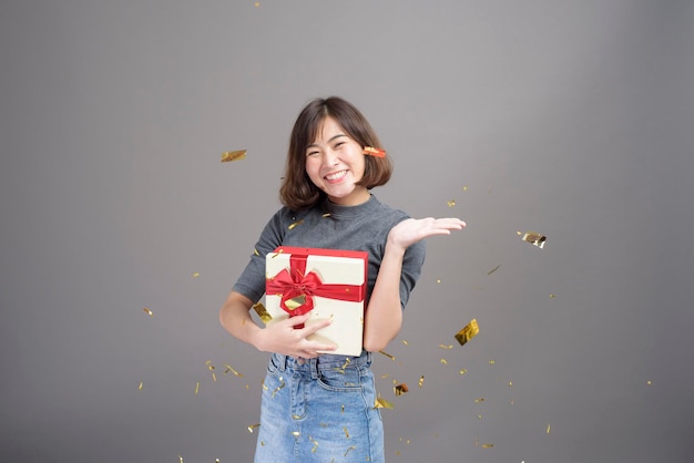 Um retrato de uma jovem linda mulher asiática comemorando e jogando papel atirar isolado estúdio de fundo cinza, Natal e ano novo conceito.