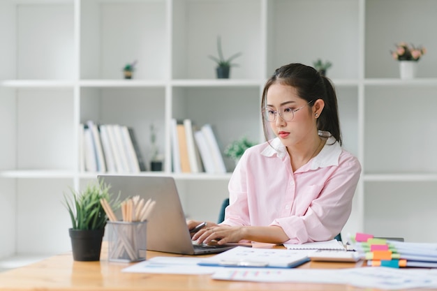 Um retrato de uma jovem sorridente, bela, profissional e confiante empresária asiática do milênio usando um laptop digital para analisar dados de vendas em um escritório moderno