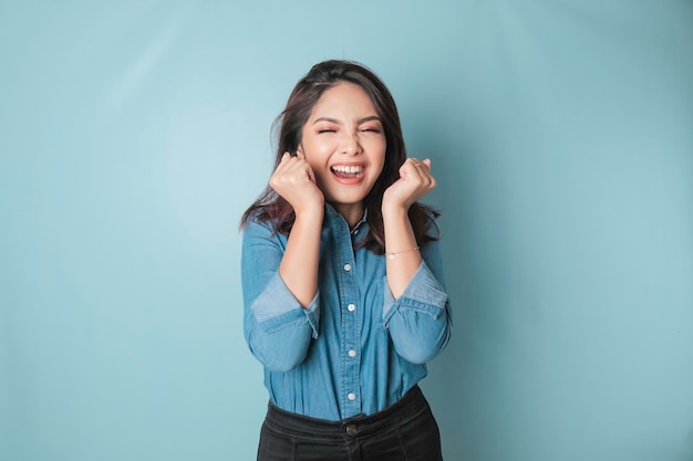 Um retrato de uma linda mulher asiática vestindo uma camisa azul e se sentindo animada e isolada por um fundo azul