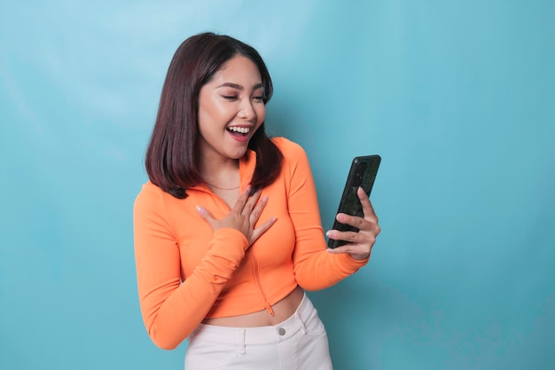 Um retrato de uma mulher asiática alegre olhando para seu smartphone sobre fundo azul
