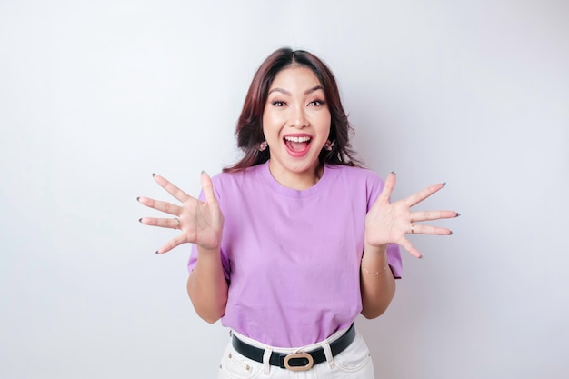 Um retrato de uma mulher asiática chocada vestindo uma camiseta roxa lilás isolada por um fundo branco