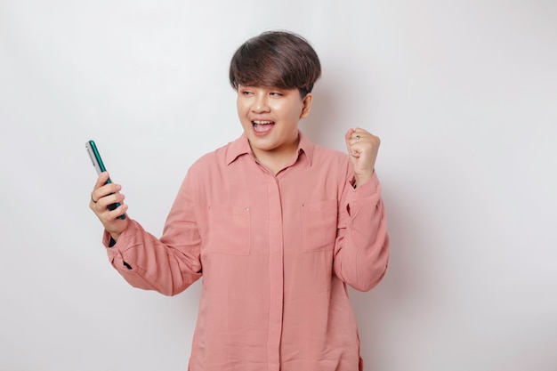 Um retrato de uma mulher asiática feliz está sorrindo e segurando seu smartphone vestindo uma camisa rosa isolada por um fundo branco