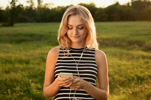 Um retrato de uma mulher bonita em pé no parque verde usando vestido listrado, segurando seu telefone celular