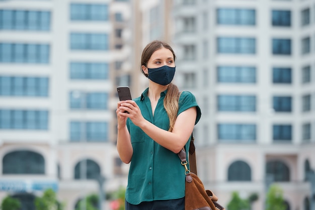 Um retrato de uma mulher em uma máscara médica está segurando um smartphone enquanto caminhava no centro da cidade