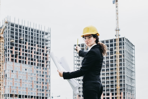 Um retrato de uma mulher engenheira olhando para a câmera. Mulher arquiteta com plano na mão e capacete amarelo com foco seleto. Engenheiro de Conceito e trabalho de negócios.