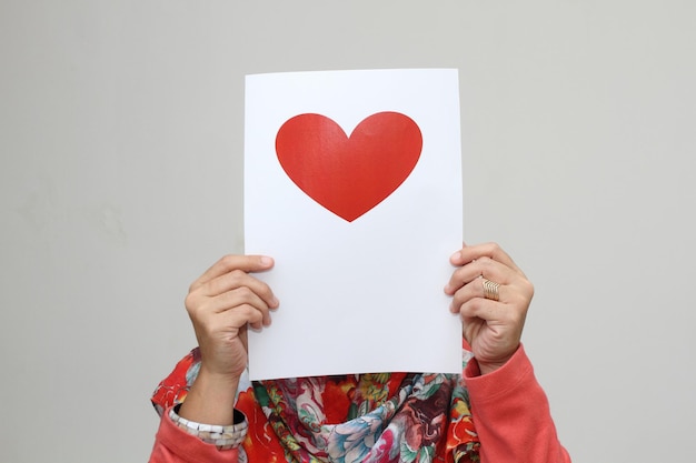 Um retrato de uma senhora cobre o rosto com um coração vermelho impresso no papel