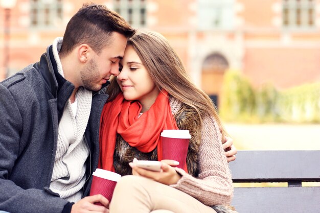 Um retrato desfocado de um jovem casal em um banco com smartphone no parque