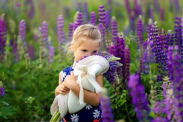 Um retrato do close-up de uma menina bonita com cabelo loiro joga em um campo de tremoço de florescência. conceito de infância. filhos e natureza.