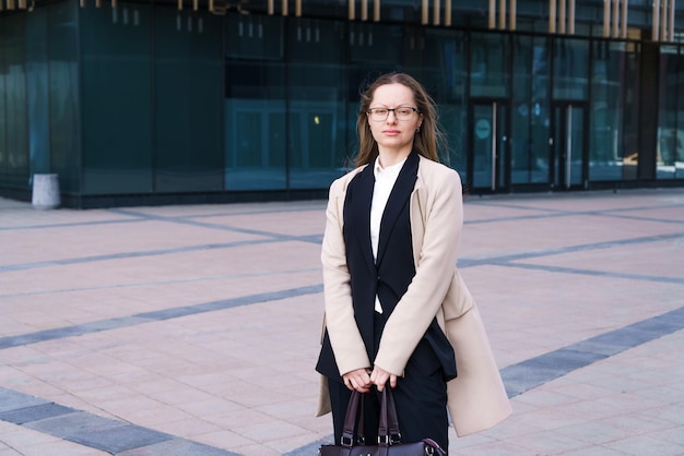 Um retrato feminino de uma mulher de negócios caucasiana em traje de negócios elegante fica em copos perto de ...