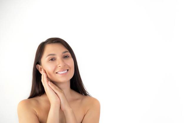 Um retrato natural de uma jovem morena bem cuidada com maquiagem nua Beleza suave mantém as mãos perto do rosto Lugar de fundo branco para texto