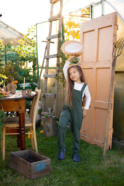 Foto um retrato vertical de uma linda e engraçada agricultora de olhos azuis com um chapéu de cabelo comprido e um macacão verde horticultura hobby lifestyle