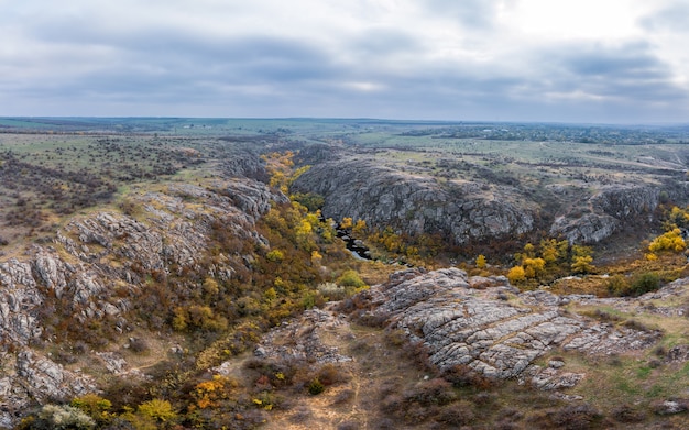 Um riacho pitoresco flui no desfiladeiro aktovsky cercado por árvores de outono e grandes rochas de pedra