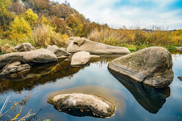 Um riacho rápido e limpo corre entre grandes pedras lisas e úmidas, cercado por pedaços altos e secos que balançam ao vento na pitoresca Ucrânia