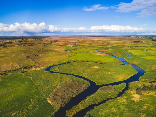 Um rio atravessa um campo verde com um céu azul e nuvens ao fundo Foto aérea do drone