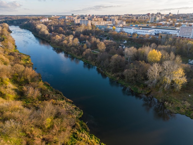 Um rio largo e calmo flui através de uma grande cidade, passando por um parque e uma floresta Paisagem de outono Vista do rio de um drone Voo de drone sobre a cidade