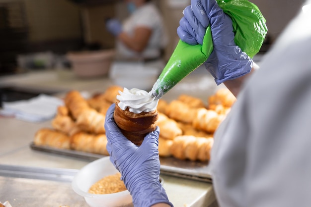 Um rolo de massa folhada doce e as mãos de um pasteleiro espalham o creme de um saco de pastelaria Assar no restaurante Proteína e creme