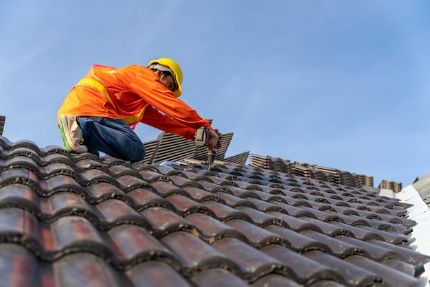 Um Roofer trabalhando na estrutura do telhado do edifício no canteiro de obras Roofer usando ar ou pistola de pregos pneumática e instalando telhas de concreto no novo telhado superior