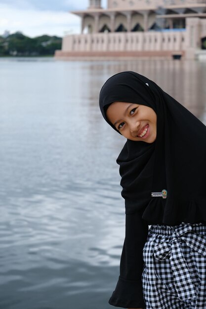 Foto um rosto feliz de uma garota asiática sentada perto do lago no marco de putrajaya, na malásia