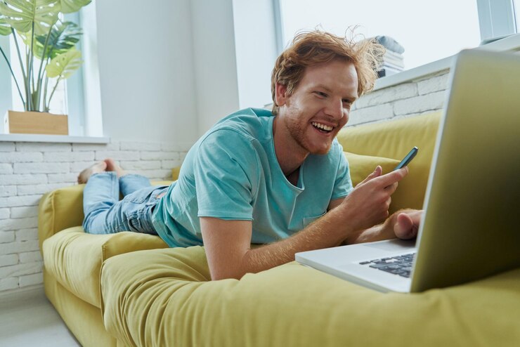 Foto um roxo alegre usando tecnologias enquanto está deitado no sofá em casa.