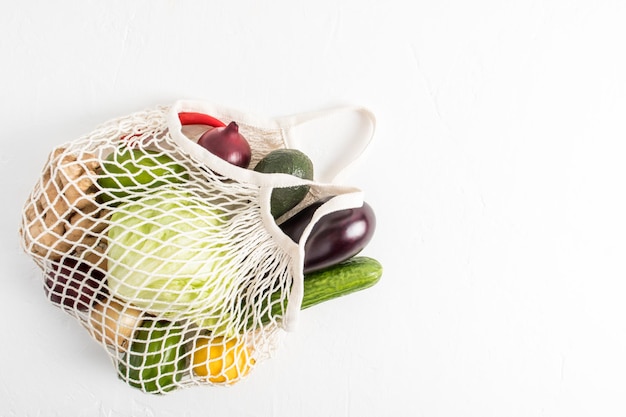 Um saco de corda branco cheio de legumes frescos em um fundo branco vista superior o conceito de comida vegana e compras sem embalagem plástica