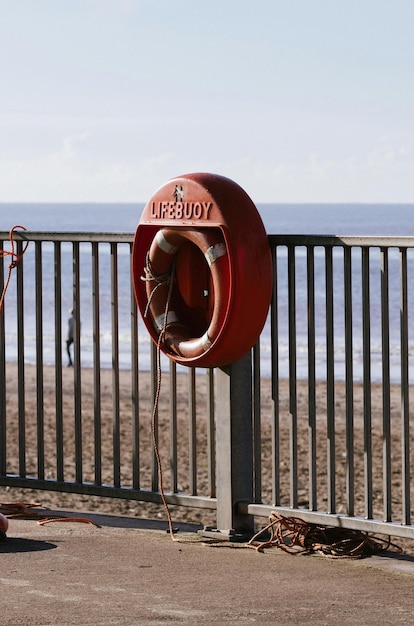 Um salva-vidas vermelho está numa cerca à beira da praia.