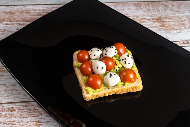 Um sanduíche de queijo e tomate em uma placa preta sobre um fundo de madeira