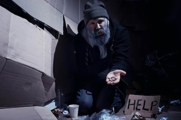Um sem-teto barbudo senta-se em caixas na rua e pede ajuda Precisa de um sem-teto pede dinheiro para comida e pernoite