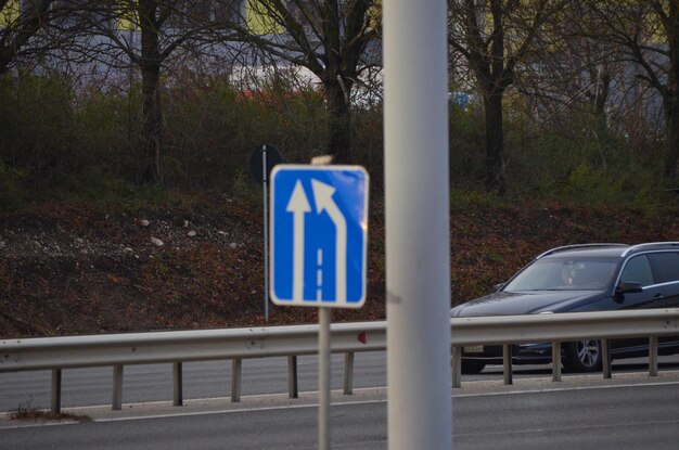 Um sinal azul com uma flecha apontando para a direita está em um poste Um carro está dirigindo pela estrada