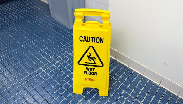 Um sinal de advertência amarelo em um piso de azulejo azul