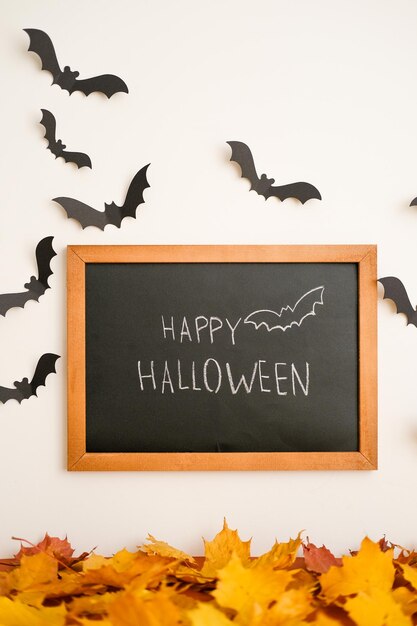 Foto um sinal dizendo feliz halloween cercado por morcego preto e folhas de laranja