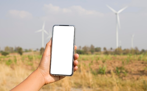 Um smartphone com uma tela branca criativa e um campo de turbinas eólicas elétricas ao fundo