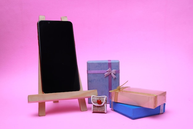 Um smartphone e algumas caixas de presente são isolados em um fundo magenta.