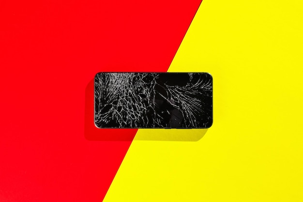 Um smartphone preto com uma tela rachada fica em um fundo vermelho e amarelo