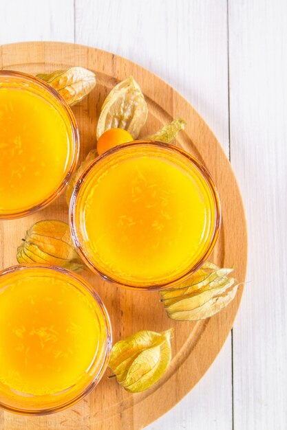 Um smoothie de laranja feito de physalis em uma mesa de madeira branca.