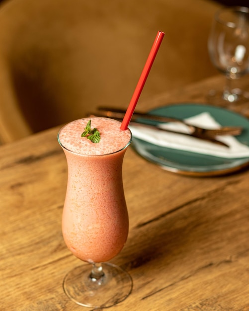 Um smoothie rosa com um canudo fica sobre uma mesa de madeira.