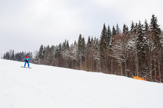 Um snowboarder masculino desce a pista ao lado de um esporte de inverno de estância de esqui de floresta nevada