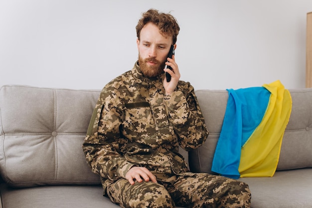Um soldado ucraniano em uniforme militar está sentado em um sofá no escritório e falando ao telefone