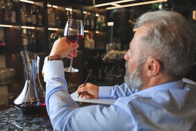 Um sommelier sênior está degustando vinho tinto.