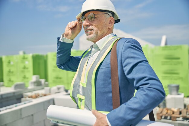 Um sonhador construtor sênior, caucasiano, do sexo masculino, com um capacete, olhando para a distância