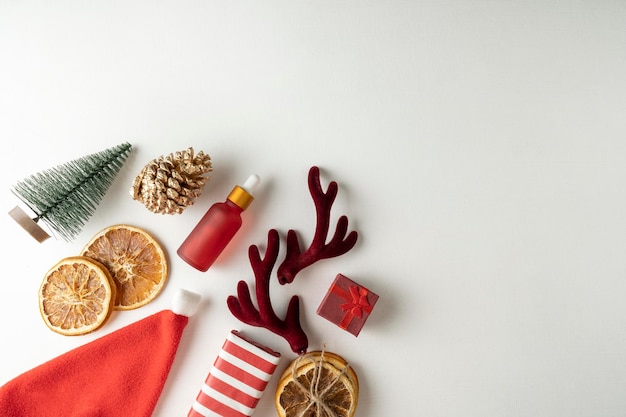 Um soro facial ou óleo essencial para férias de Natal em um frasco conta-gotas vermelho sobre um fundo branco com canela e laranjas secas ao redor