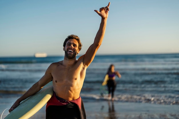 Um surfista feliz gesticulando e cumprimentando enquanto sorri para a câmera