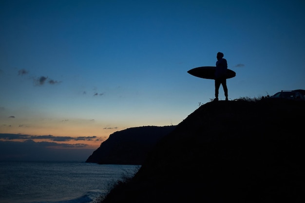 Um surfista fica na luz do pôr do sol depois de pedalar