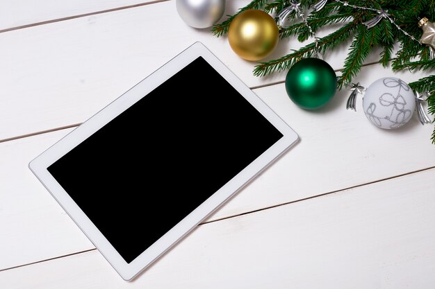 Um tablet branco com espaço para copiar em uma mesa de madeira com galhos de pinheiro e bolas de Natal